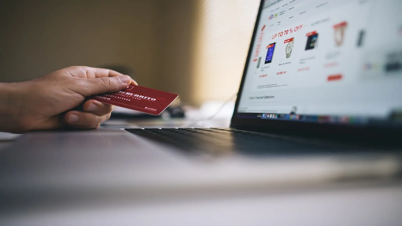 E-commerce shopping experience Hand holding up a credit card next to an e-commerce platform on a laptop screen.